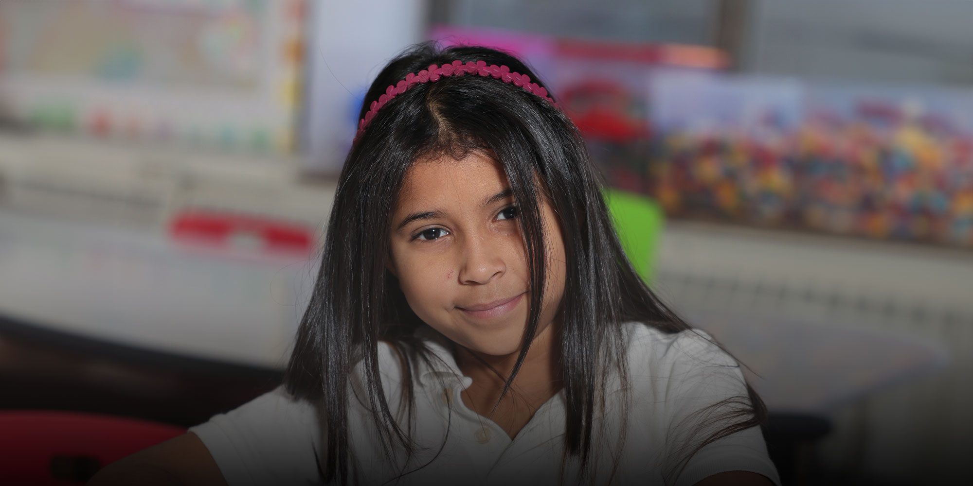 Student with a pink headband sitting at a desk in a classroom.