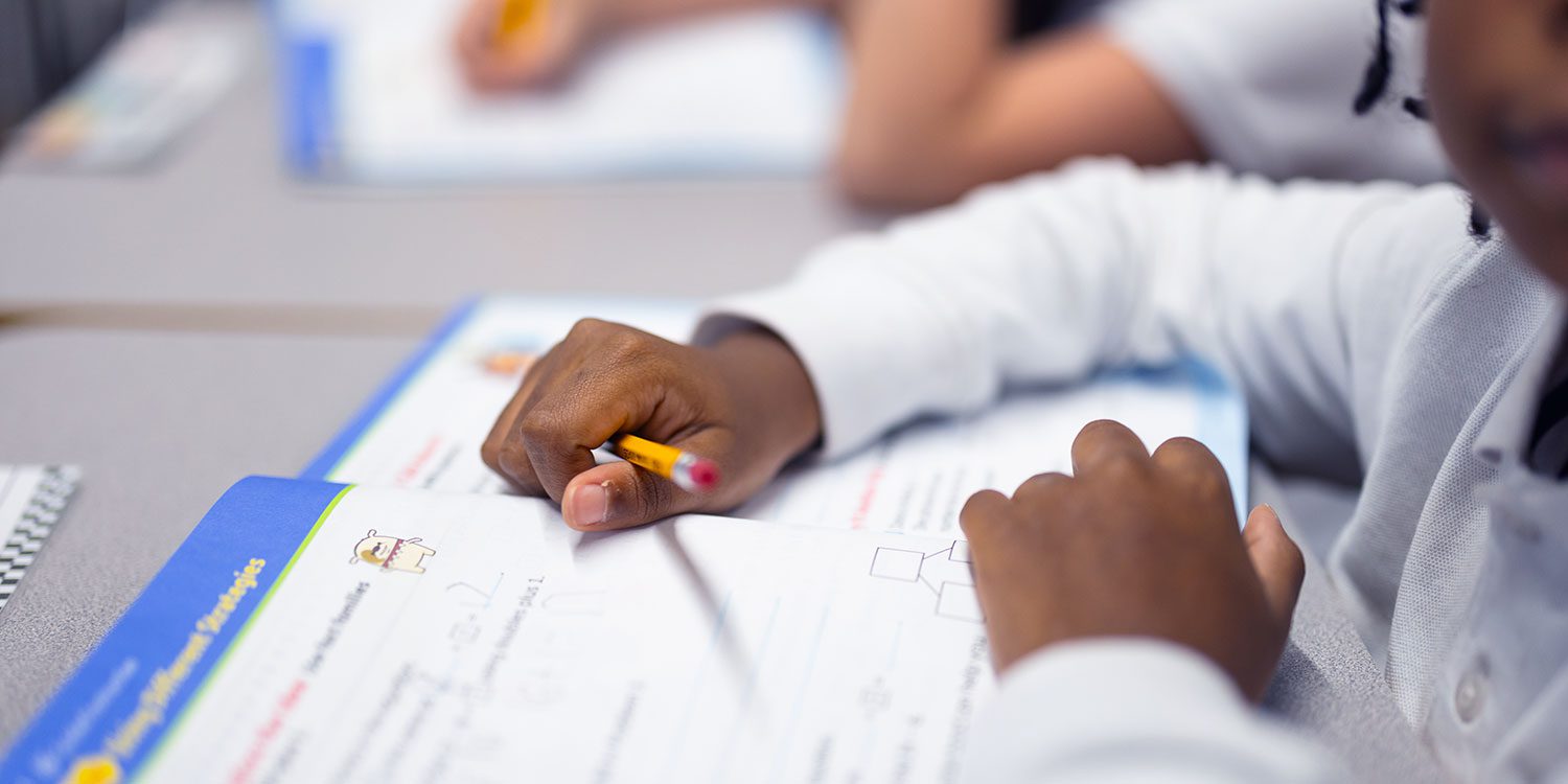 Student holding a pencil over an open math workbook.