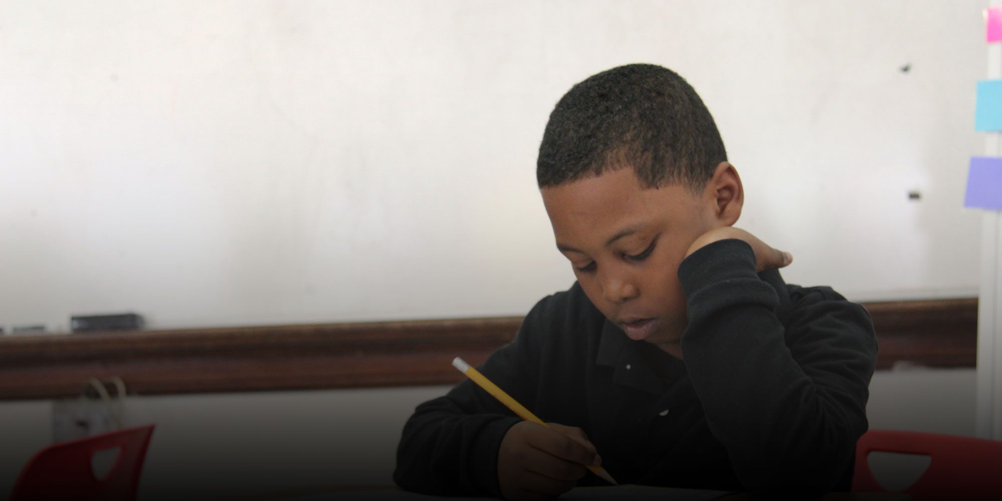 Student writing with a pencil at a desk.