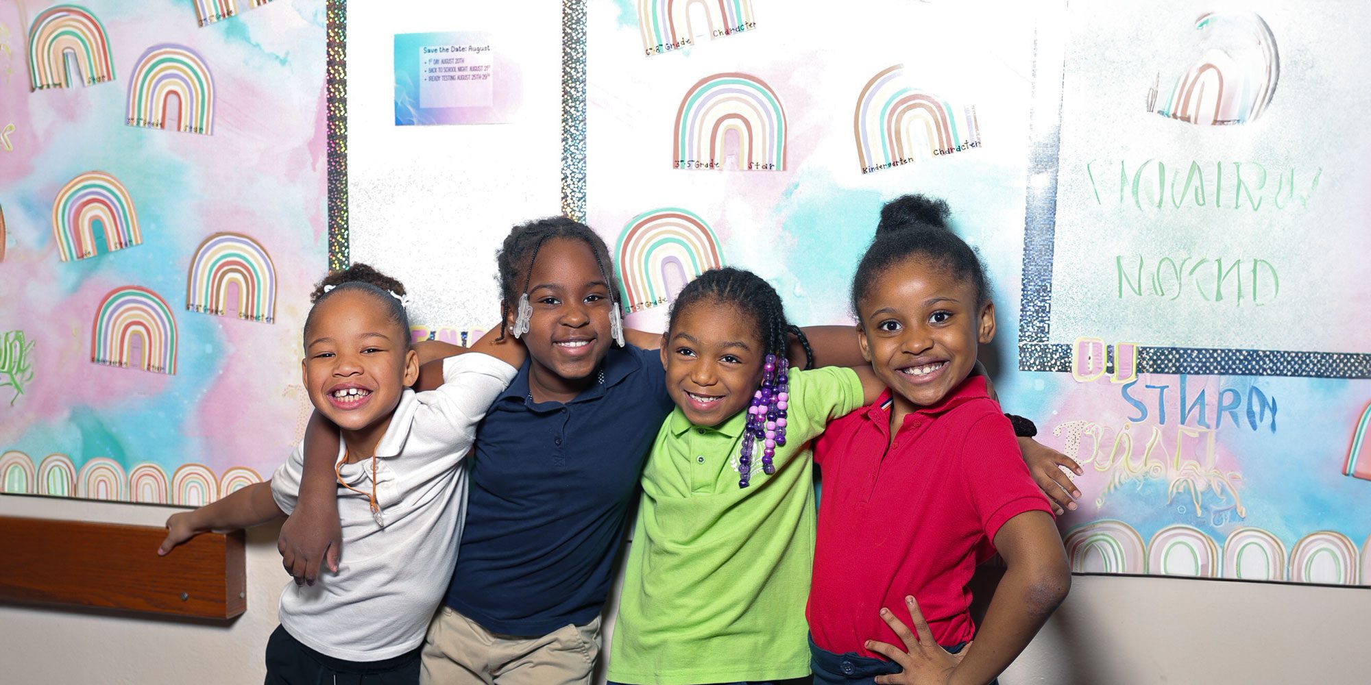 Four smiling students with arms around each other in a school hallway.
